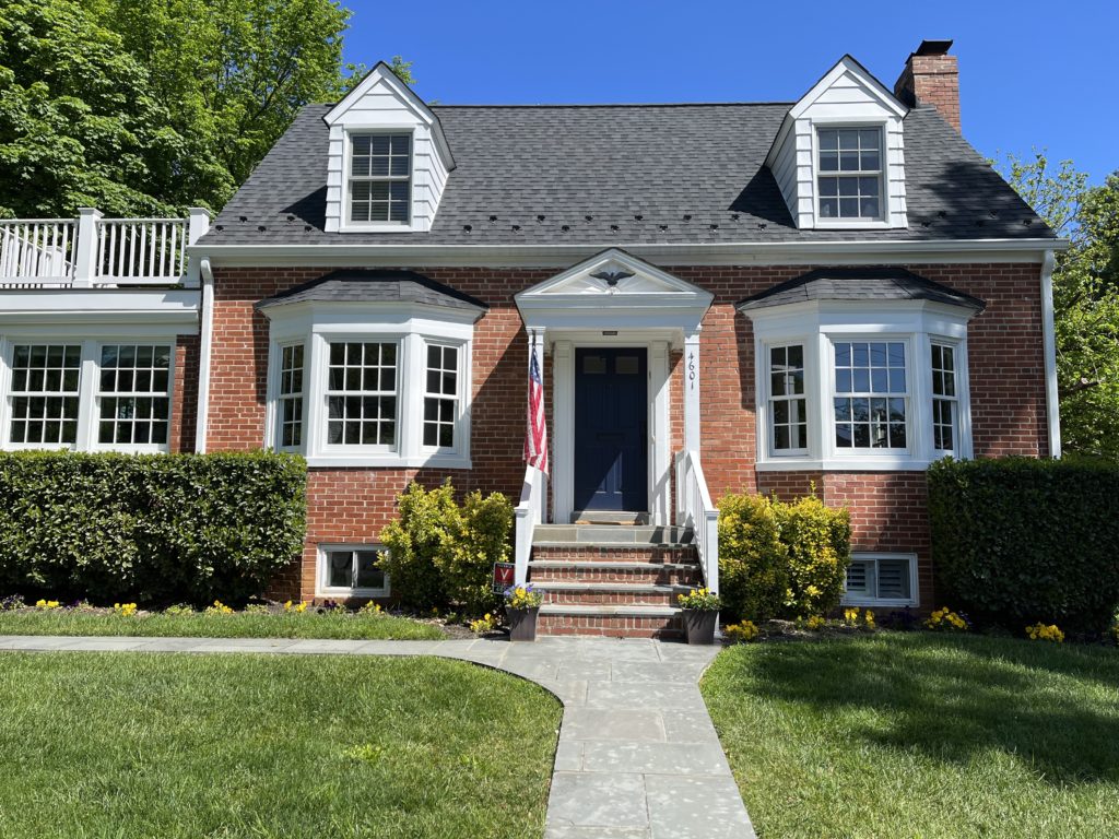 A two-story brick house with a mowed front yard. There are walkways leading to a small staircase that goes to the front entryway of the house.